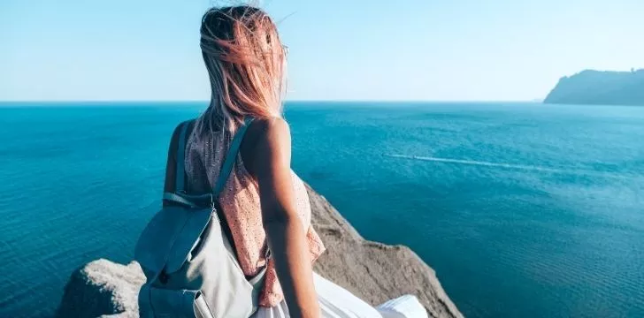 A woman standing on a rock looking across the wide blue ocean