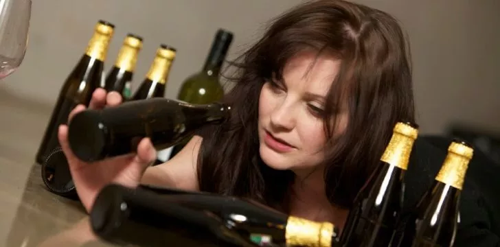 A woman looking for the last drop of wine in a bottle to cure her hangover